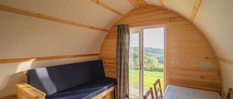 Une pièce chaleureuse avec un plafond en bois, un banc doté d’un coussin foncé, une table recouverte d’une nappe à motifs et une vue sur la verdure à travers une porte vitrée.