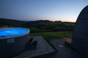 Un jacuzzi en una terraza de madera con vista a un cerro boscoso.