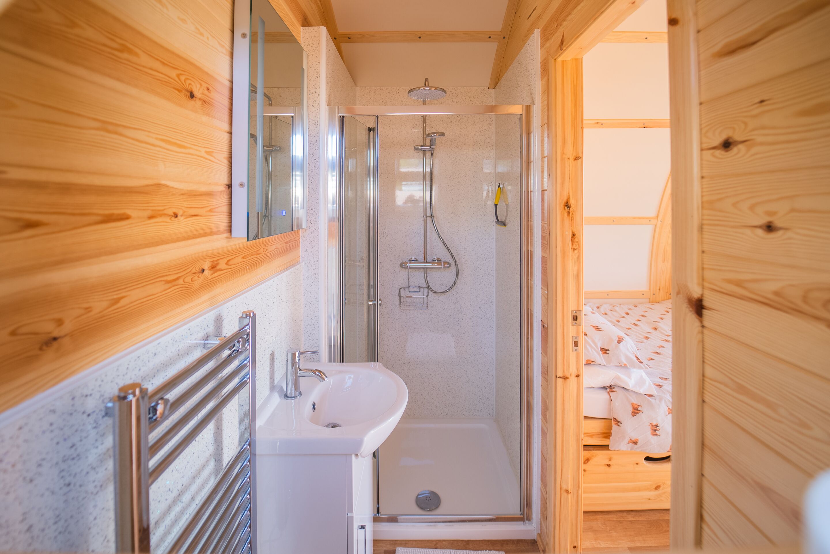 L’intérieur d’un chalet en bois comprend une douche, un lavabo et un lit avec une literie à motifs.