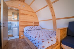 Una habitación de madera con una cama, una mesita de noche y una puerta que da a un baño.