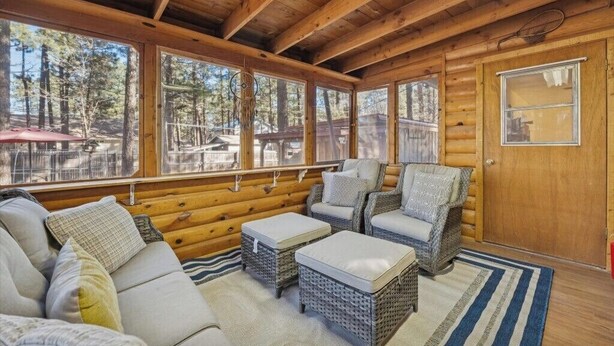L’intérieur d’une cabane en rondins, avec un canapé, des fauteuils en osier et une vue sur la forêt à travers de grandes fenêtres.
