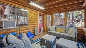 L’intérieur d’une cabane en rondins, avec un canapé, des fauteuils, une petite table et une fenêtre.