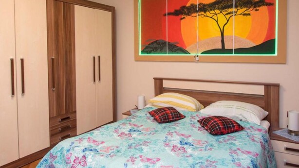 Un dormitorio con cama, almohadas, mesita de noche, armario y un cuadro colgado en la pared.