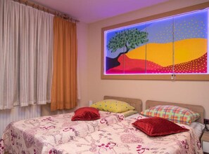 A bedroom with a bed, curtains, a wall-mounted artwork, and a nightstand.
