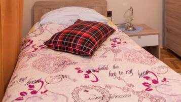 A bed with a patterned bedspread, a red plaid pillow, a bedside lamp, and a nightstand.