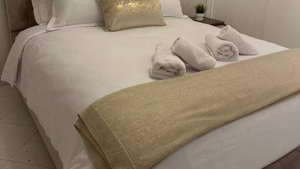 Una cama bien hecha con un cabecero capitonado, ropa de cama blanca y una almohada decorativa dorada.