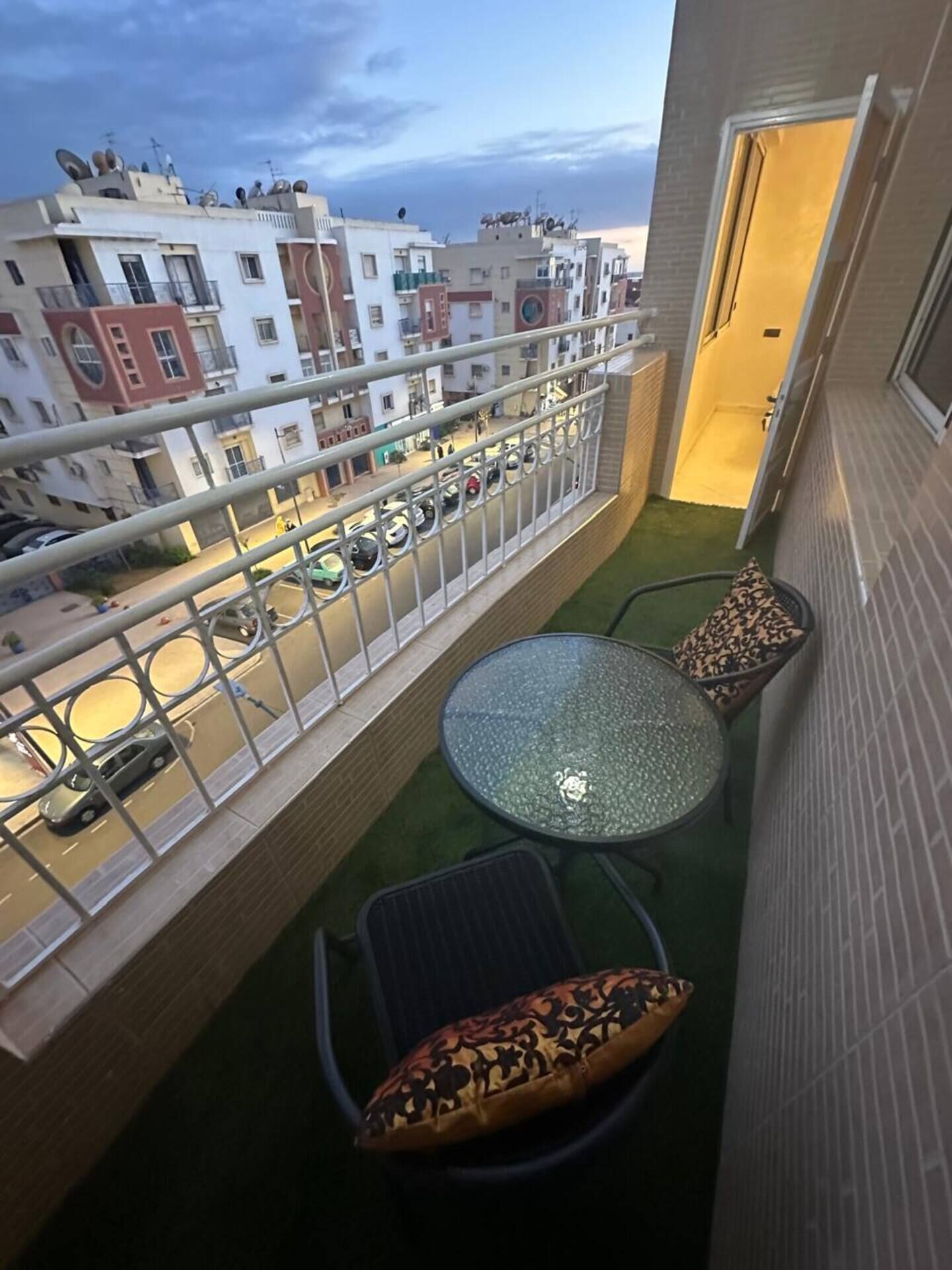 A balcony with a glass table, two chairs, and patterned cushions.