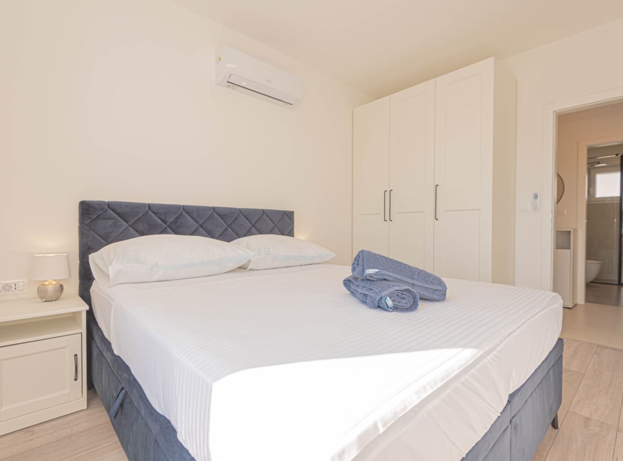A bedroom with a bed, a nightstand, a wardrobe, and an air conditioning unit.
