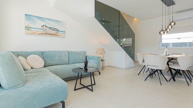 A modern living room with a sofa, a dining table with chairs, a staircase, and a painting on the wall. - Villa Pomalo (Vodice)