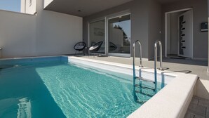 A swimming pool with clear water, two lounge chairs, and a glass door leading to a covered area. - Villa Pomalo (Vodice)