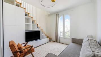 A modern living room with a flat-screen TV, a sofa, a chair, and a staircase.