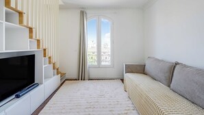 A living room with a TV, sofa, staircase, and a window with curtains. - Charming Duplex 2br/6p - Aubervilliers (Aubervilliers)