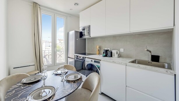 A compact kitchen with a dining area, including a table set for two, a microwave, a washing machine, and a sink. - Charming Duplex 2br/6p - Aubervilliers (Aubervilliers)