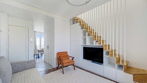 A modern living room with a sofa, a chair, a TV, and a unique wooden staircase. - Charming Duplex 2br/6p - Aubervilliers (Aubervilliers)