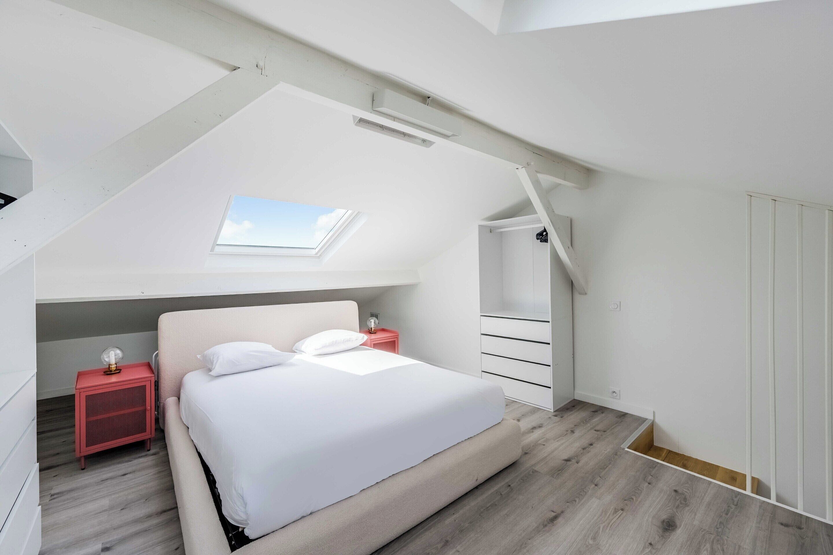 A bedroom with a skylight, a bed, a nightstand, and a wardrobe.