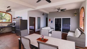 A spacious living area with a dining table, two sofas, a kitchen area with a refrigerator, and a ceiling fan. - Casa Moonbeam (Yelapa)