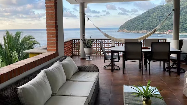 A covered outdoor seating area with a view of the sea, a hammock, and a table with chairs. - Casa Moonbeam (Yelapa)