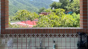 A kitchen with a sink, a coffee maker, and a view of a mountainous landscape through an arched window. - Casa Moonbeam (Yelapa)