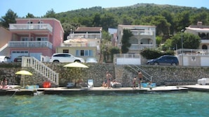 Ein Hotel an der Küste mit Schwimmbad, Steinmauern und Blick auf Meer und Hügel.