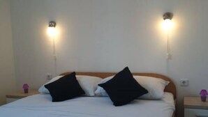 Ein Bett mit weißer Bettwäsche und schwarzen Kissen, zwei Nachttische mit Lampen und ein Holzkopfstück.