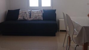 Ein Zimmer mit einem dunkelgrauen Sofa, einem kleinen Tisch und einem Fenster.