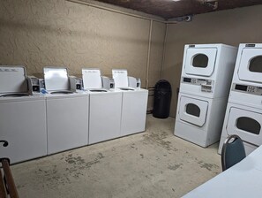A laundry room with multiple washing machines and dryers, a trash bin, and a concrete floor. - Luxury Beachfront Condo: King Suite in Premier Location in North Myrtle Beach (North Myrtle Beach)