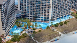 A high-rise hotel with multiple balconies, a central swimming pool, and a beach area. - Luxury Beachfront Condo: King Suite in Premier Location in North Myrtle Beach (North Myrtle Beach)