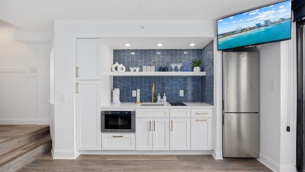A modern kitchen with white cabinets, a stainless steel refrigerator, a built-in oven, and a blue-tiled backsplash. - Luxury Beachfront Condo: King Suite in Premier Location in North Myrtle Beach (North Myrtle Beach)