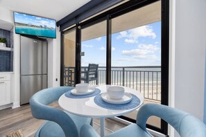A balcony with a TV, a table with two bowls, and a view of the beach. - Luxury Beachfront Condo: King Suite in Premier Location in North Myrtle Beach (North Myrtle Beach)
