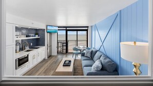A modern living room with a sofa, a TV, and a balcony with a view. - Luxury Beachfront Condo: King Suite in Premier Location in North Myrtle Beach (North Myrtle Beach)