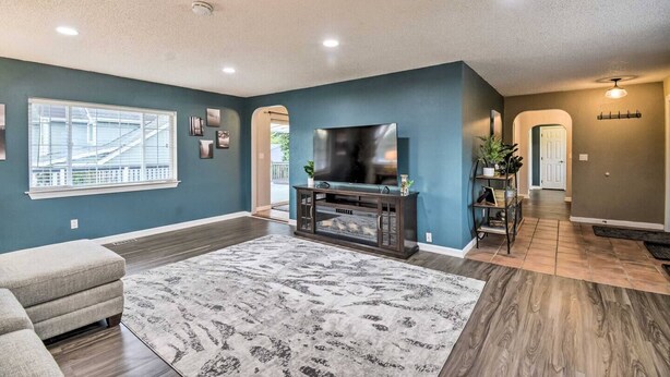 A living room with a large flat-screen TV, dark wood flooring, a patterned rug, and a grey sofa. - Spacious, Cozy 3 Bedroom 2 bath North End Home (Tacoma)