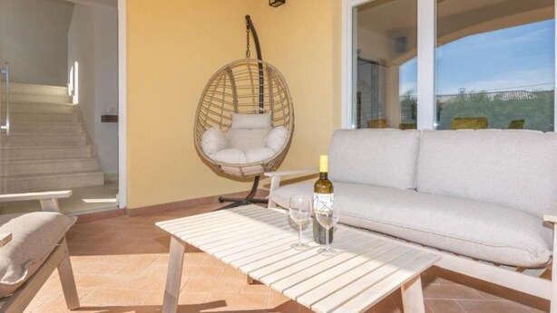 Un patio soleado con una mecedora, un sofá y una mesa con una botella y una copa.