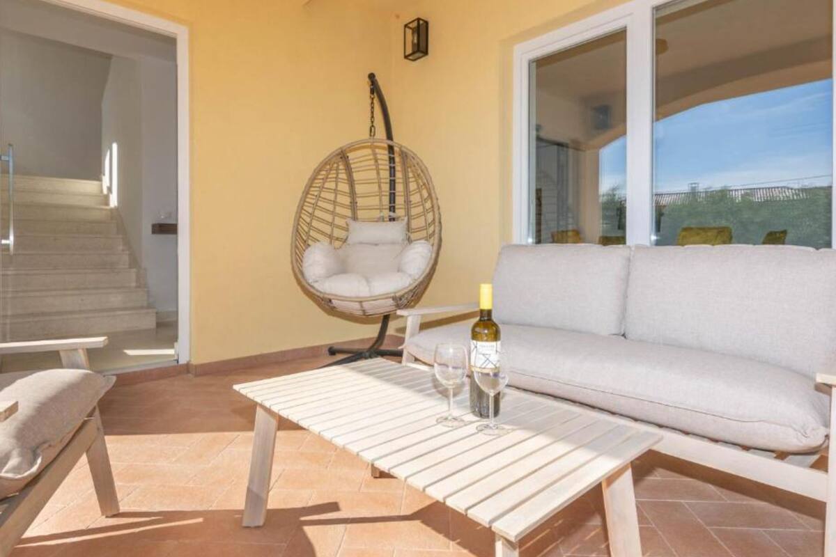 Un patio soleado con una mecedora, un sofá y una mesa con una botella y una copa.