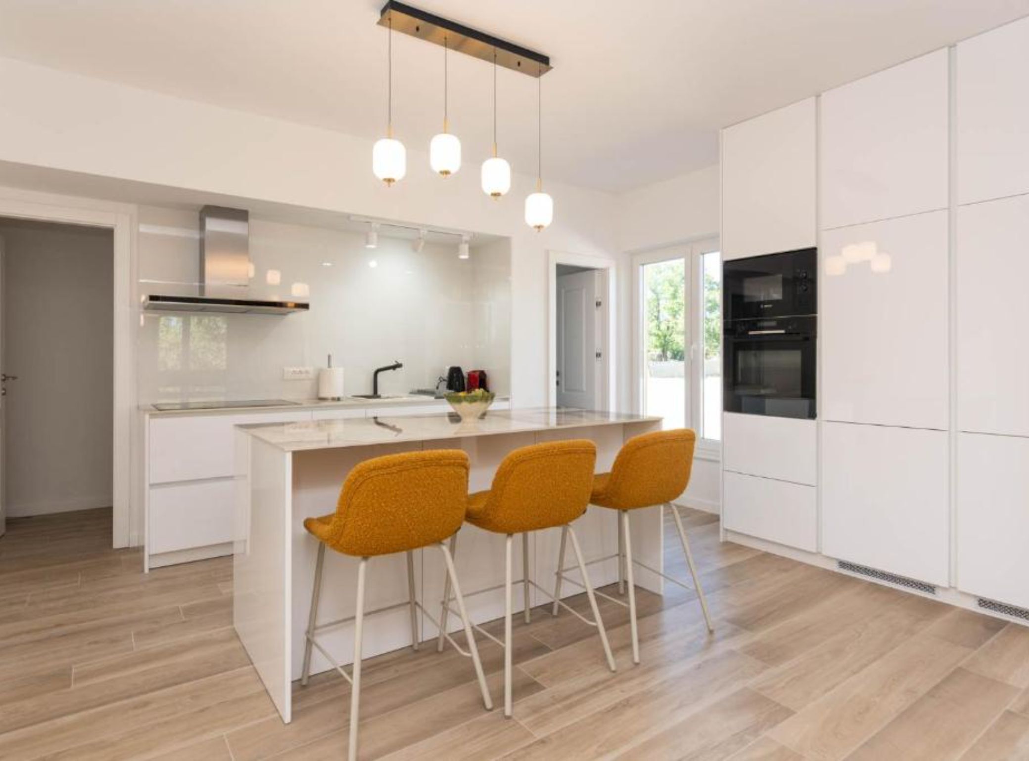 Una cocina moderna con una isla central, muebles blancos y una zona de bar con sillas amarillas.