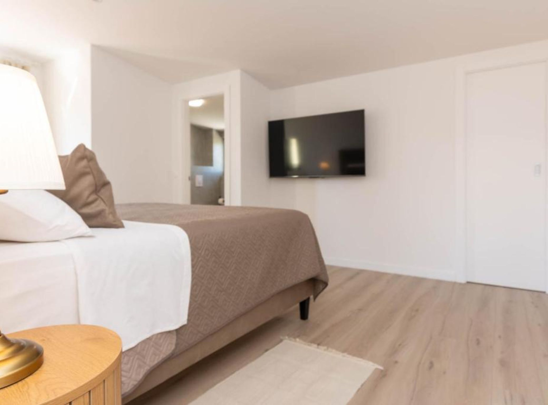 Un dormitorio moderno con una cama, un televisor montado en la pared y piso de madera.