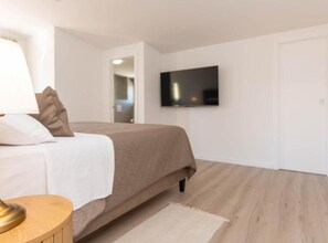 A modern bedroom with a bed, a TV mounted on the wall, and a wooden floor.