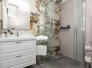 A bathroom with a white vanity, a glass shower enclosure, and a marble wall.