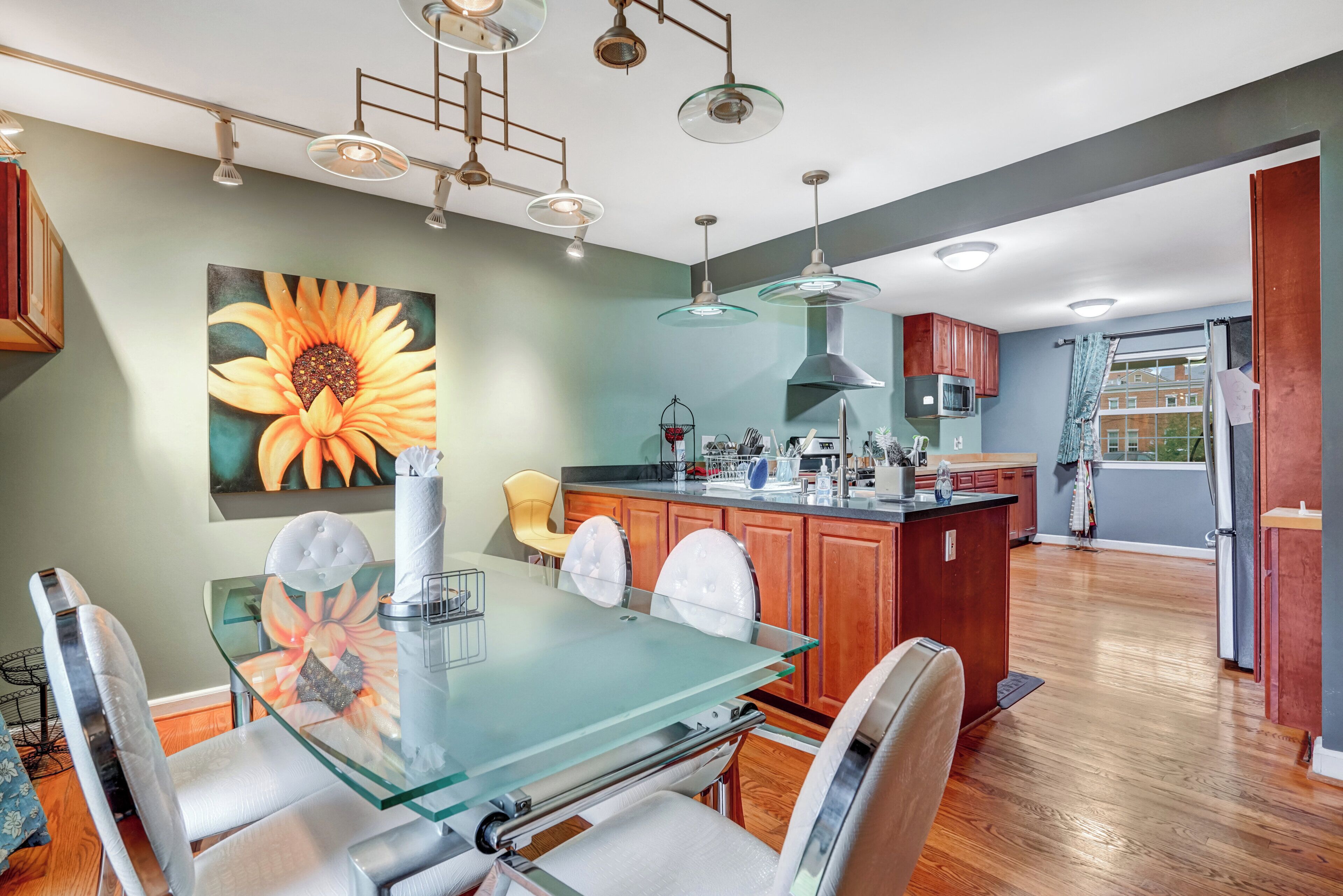 A modern kitchen with a glass dining table, wooden cabinets, and pendant lighting.