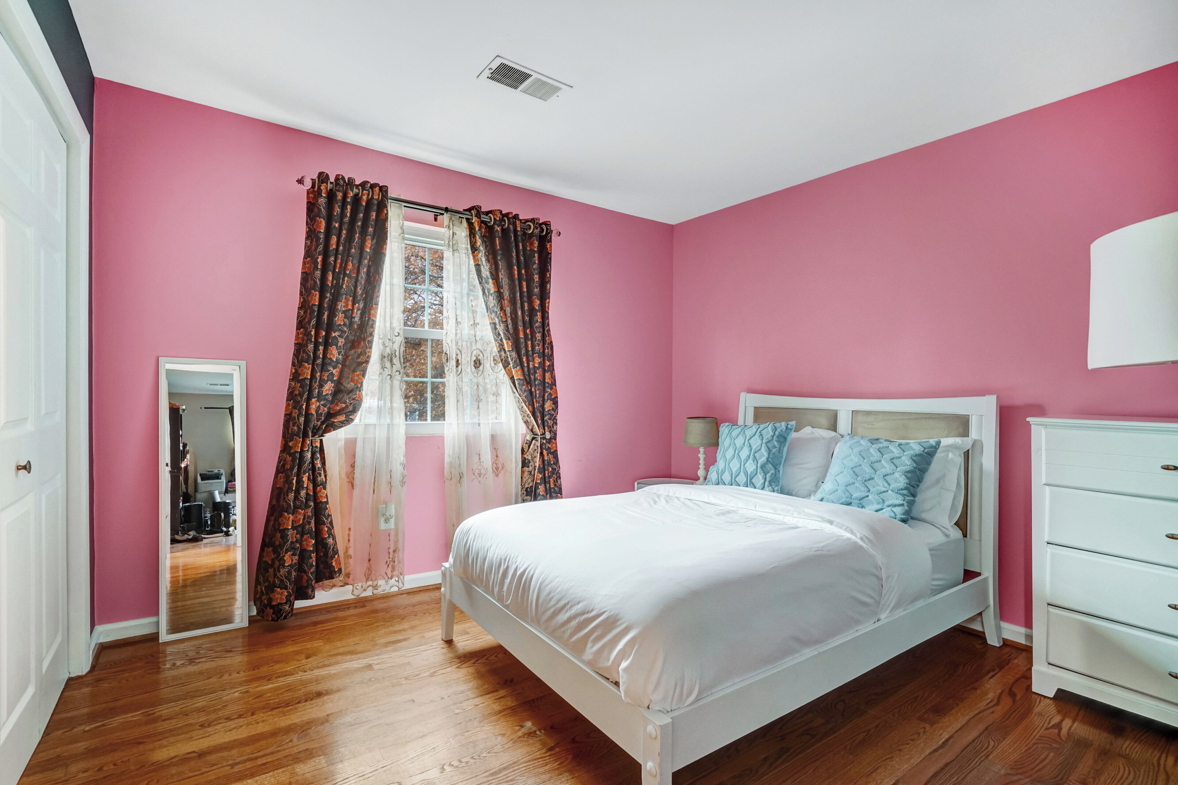 Een slaapkamer met een wit bed, roze wanden en een houten vloer.