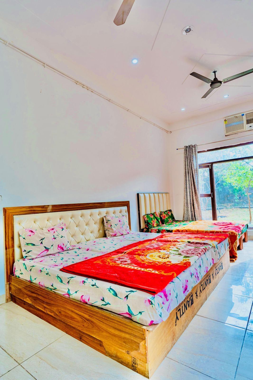 Une chambre d’hôtel avec un grand lit, un ventilateur de plafond, un appareil de climatisation et une fenêtre donnant sur un paysage verdoyant.