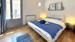 Un dormitorio con una cama grande, una mesita de noche, un reloj de pared y una ventana con cortinas.