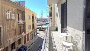 Un balcón con vista a un puerto deportivo, una calle con coches aparcados y edificios colindantes.