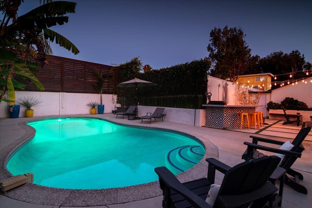 A swimming pool with lounge chairs, a bar area, and string lights.