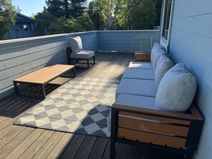 Eine Terrasse mit kariertem Teppich, einer Holzbank, einer Couch mit Kissen und einem kleinen Tisch.
