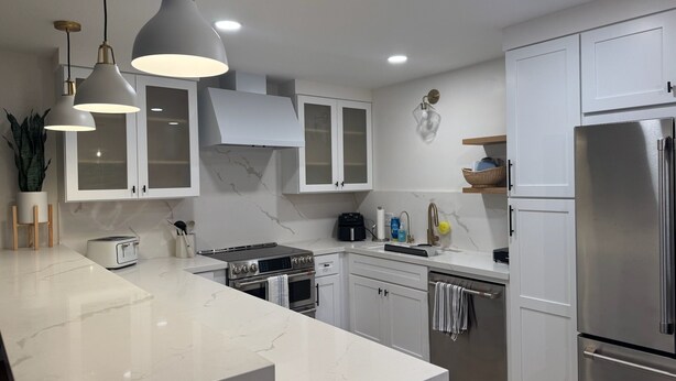 Een moderne keuken met witte kasten, een roestvrijstalen koelkast, een gasfornuis en hanglampen.