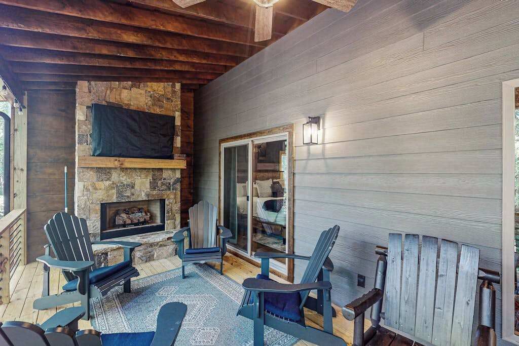 A covered patio area with Adirondack chairs, a stone fireplace, and a glass door leading to an interior space.