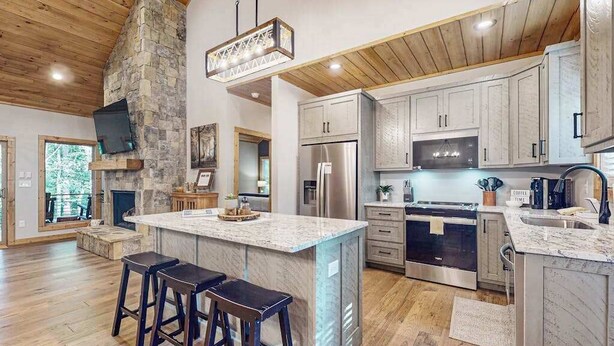 Un'ampia cucina con una grande isola, soffitto in legno, parete decorata in pietra e elettrodomestici moderni.