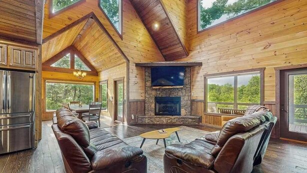 Un salón amplio con chimenea de piedra, sofás de cuero y grandes ventanales con vistas al exterior.