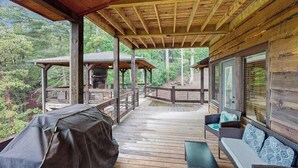 Una terraza cubierta con mobiliario exterior, una parrilla y vistas al bosque circundante.