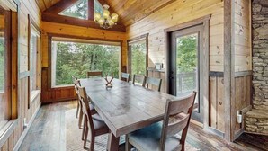 Un comedor de madera con una mesa grande y sillas, ventanas amplias y una pared de piedra.